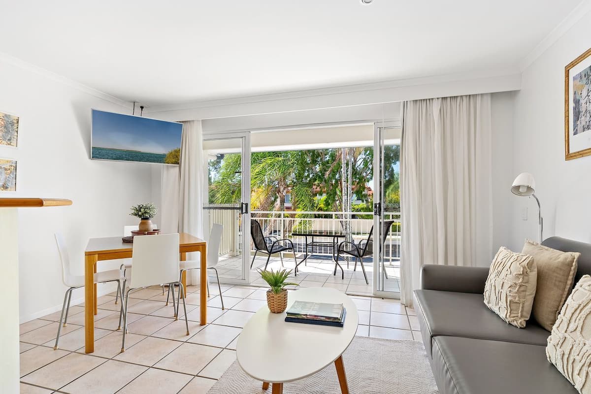 Un salon moderne comprenant un coin repas, un balcon avec vue sur la verdure et un canapé agrémenté de coussins décoratifs.