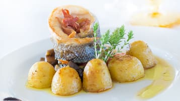 A seafood dish with a fish head, bacon, and potatoes on a white plate.