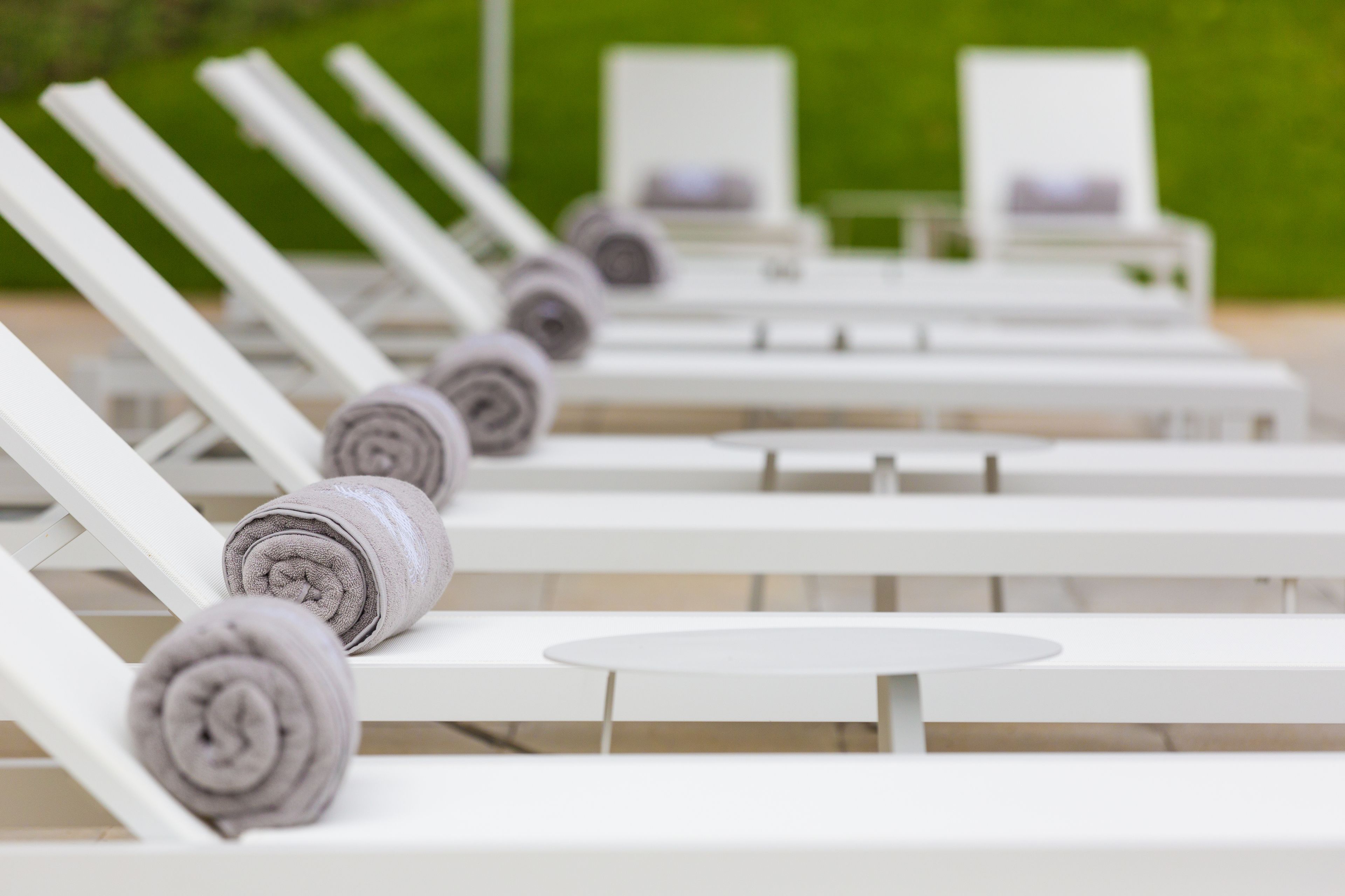 A row of white lounge chairs with towels, arranged outdoors with a green background.