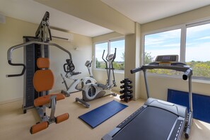 A gym with exercise equipment, a treadmill, and a view of greenery through large windows.