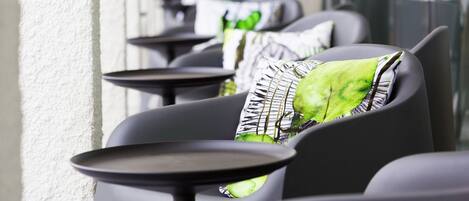 A row of outdoor seating with tables and chairs, each with a green patterned pillow.