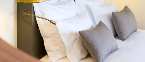 A neatly made bed with white and gray pillows, a striped lamp, and a geometric wall art piece.