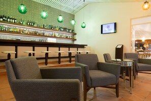 A bar area with patterned chairs, a bar counter with bottles, and hanging green globes.