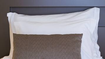 A neatly made bed with white and brown pillows, a dark headboard, and a geometric wall art piece above.