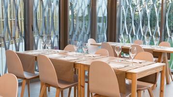Un espace repas avec des tables et des chaises en bois, de grandes fenêtres donnant sur un paysage verdoyant et un aménagement intérieur moderne.