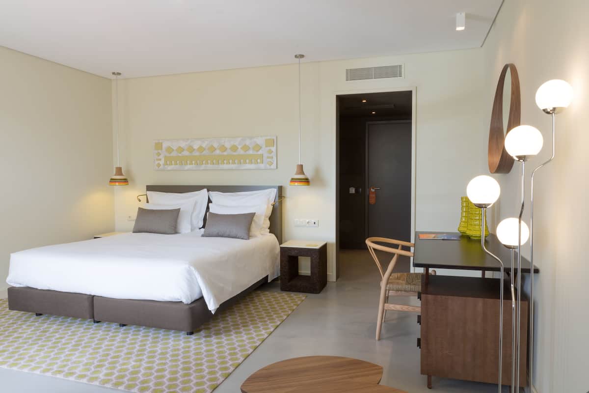 A modern bedroom with a bed, bedside tables, a desk, and a mirror with lights.
