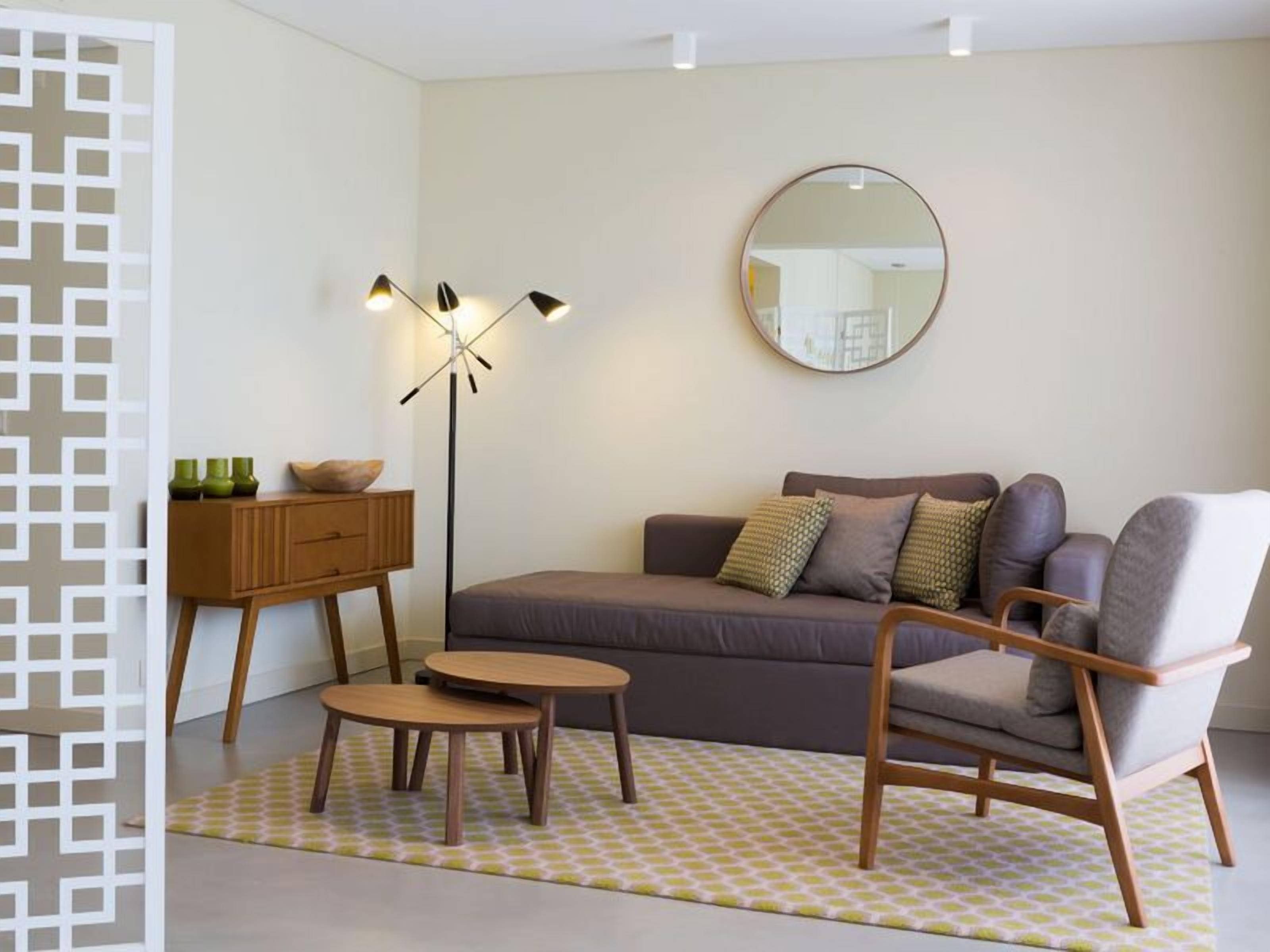 A modern living room with a sofa, a chair, a small table, a floor lamp, and a mirror on the wall.
