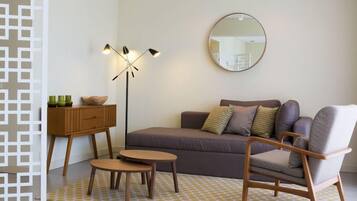 A modern living room with a sofa, a chair, a small table, a floor lamp, and a mirror on the wall.