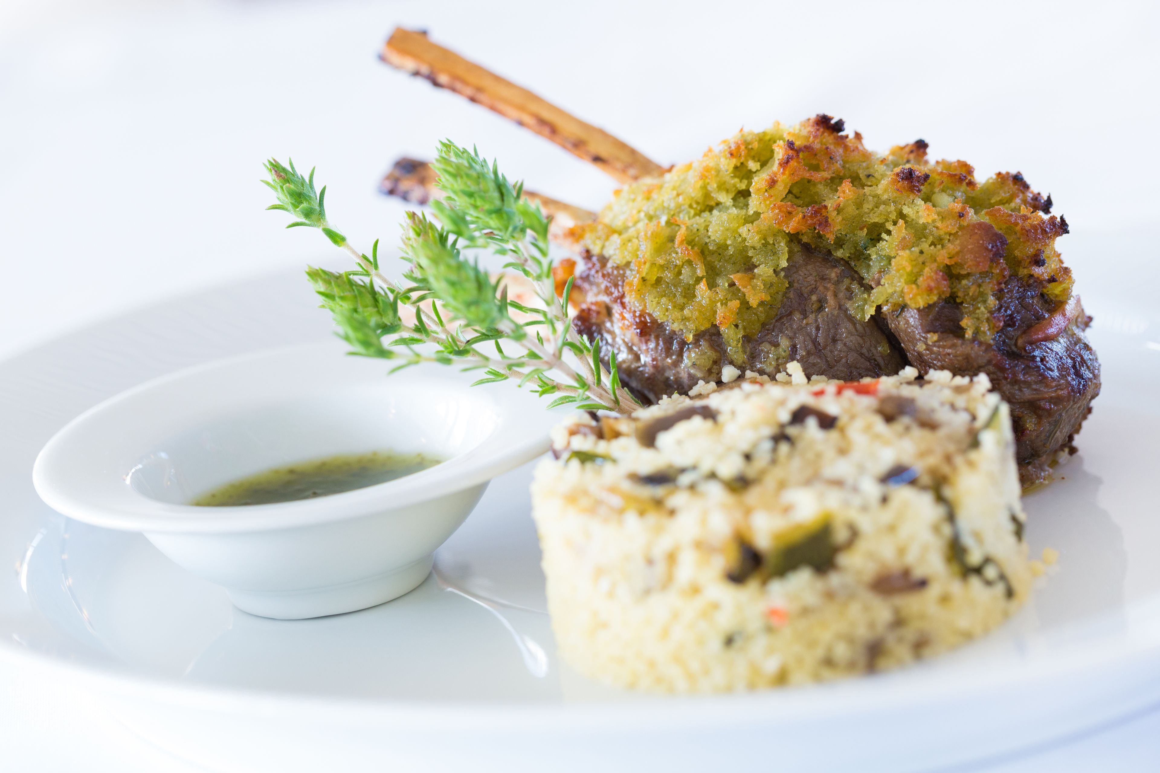 A plate with a lamb shank, a side of rice, and a small bowl of sauce.