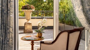 Un balcon avec une chaise, une table ornée d’un vase de fleurs et une plante en pot aux fleurs rouges.