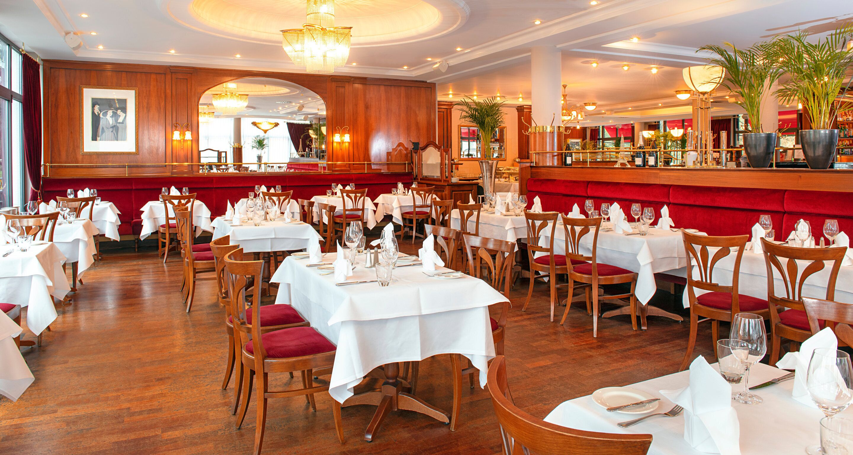 Un restaurante con varias mesas dispuestas para comer, sillas de madera y un banco con cojín rojo.