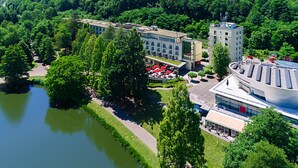 Vue aérienne d’un complexe immobilier moderne doté d’une cour centrale, entouré d’une végétation luxuriante et bordé d’une étendue d’eau.