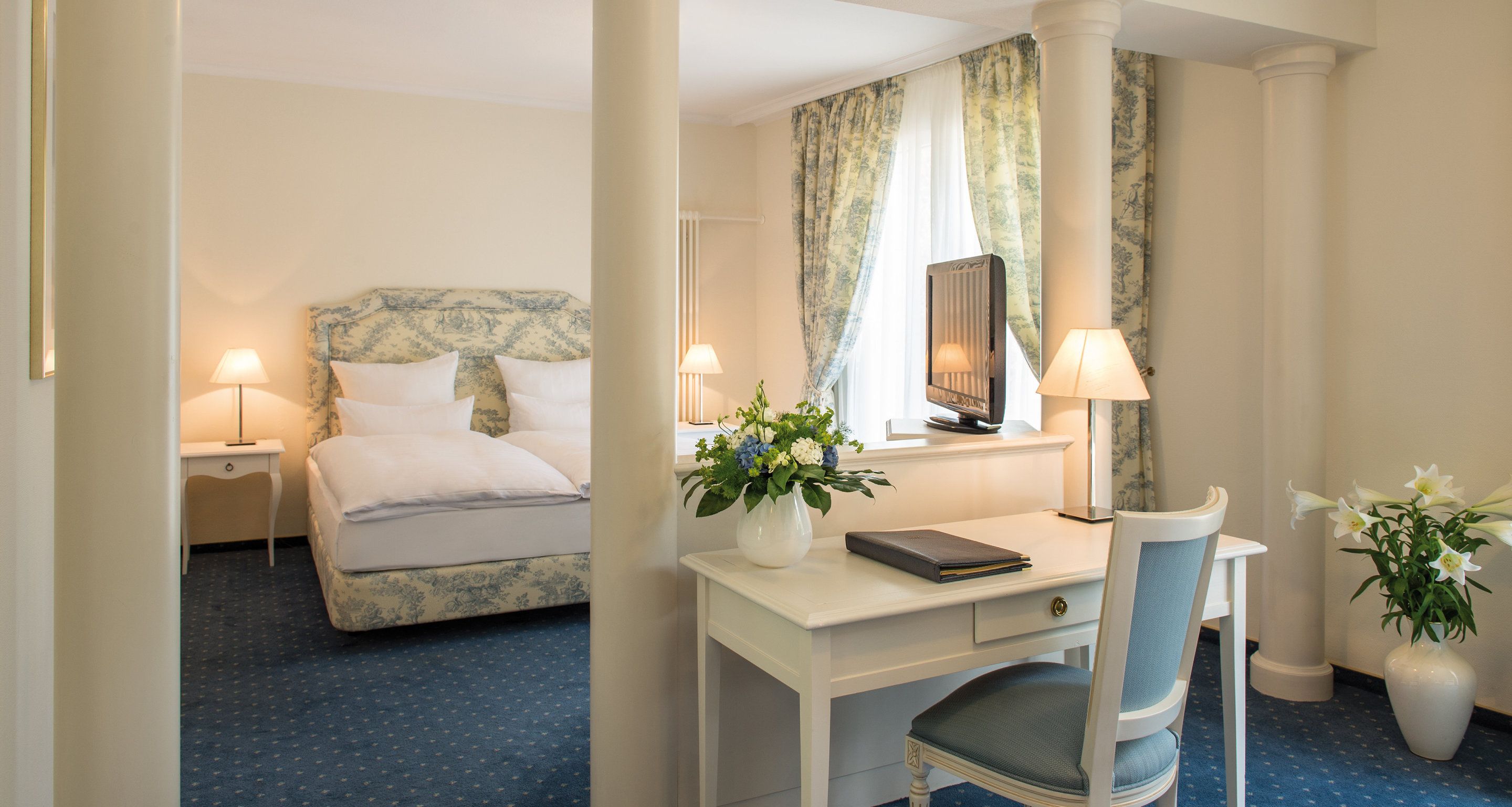 A hotel room with a bed, a desk, a chair, and two lamps.