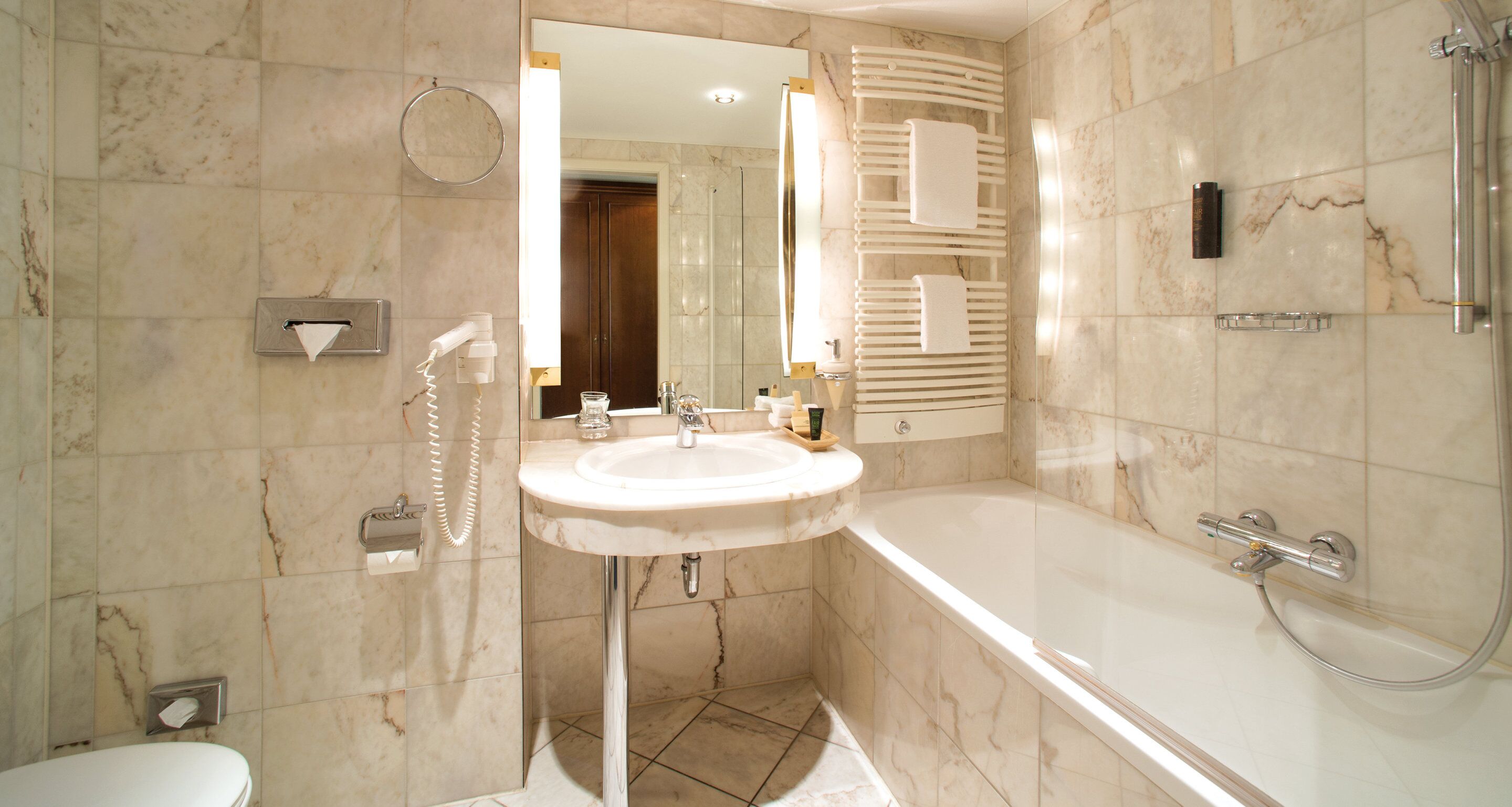 Une salle de bain avec un lavabo en marbre, un miroir, un porte-serviettes, une douche et des toilettes.