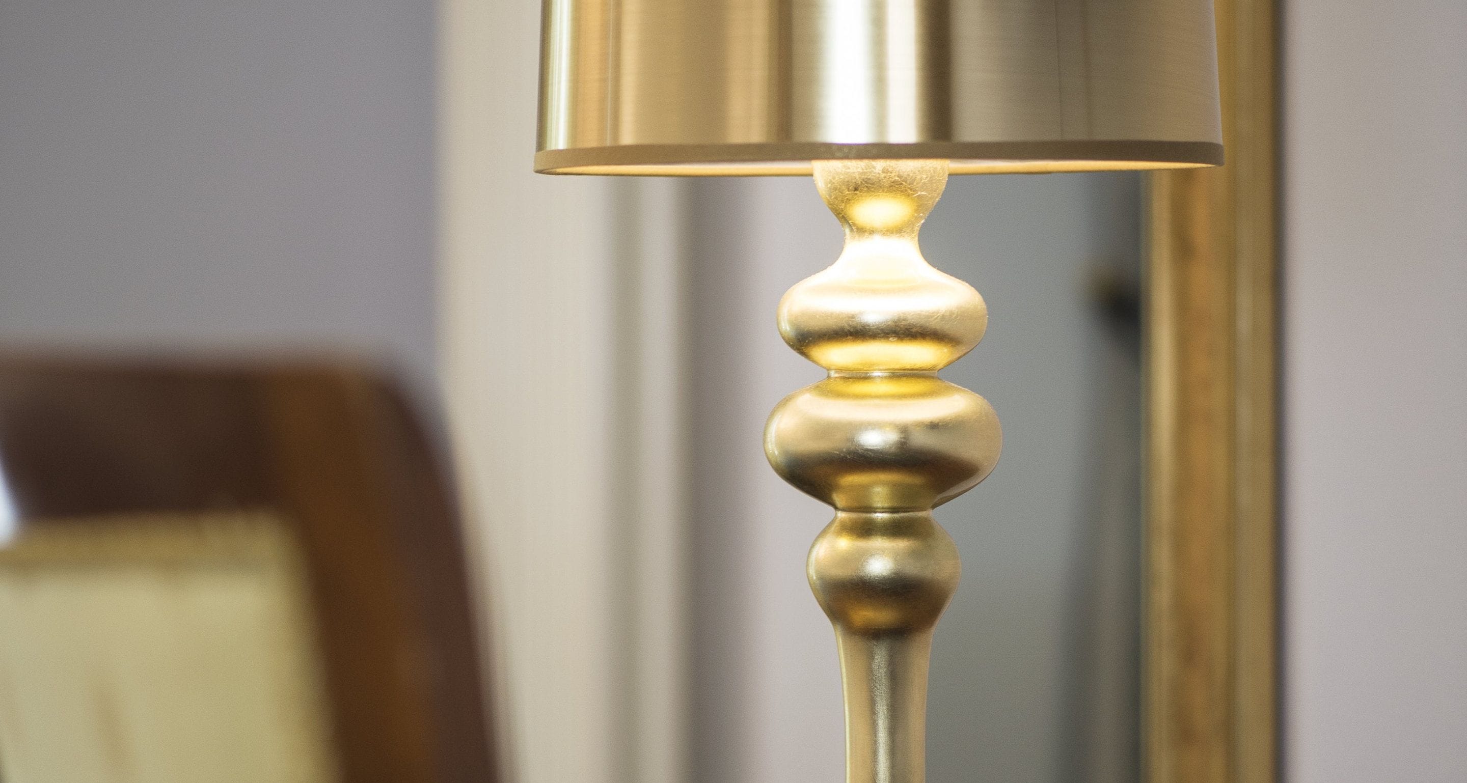 A close-up of a metallic lamp with a decorative base and a cylindrical shade.
