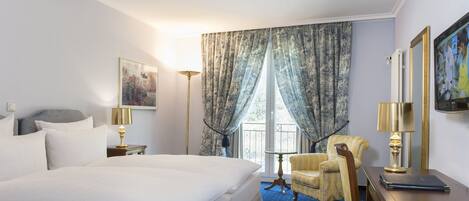 A hotel room with a large bed, a chair, a desk, and a window with curtains.