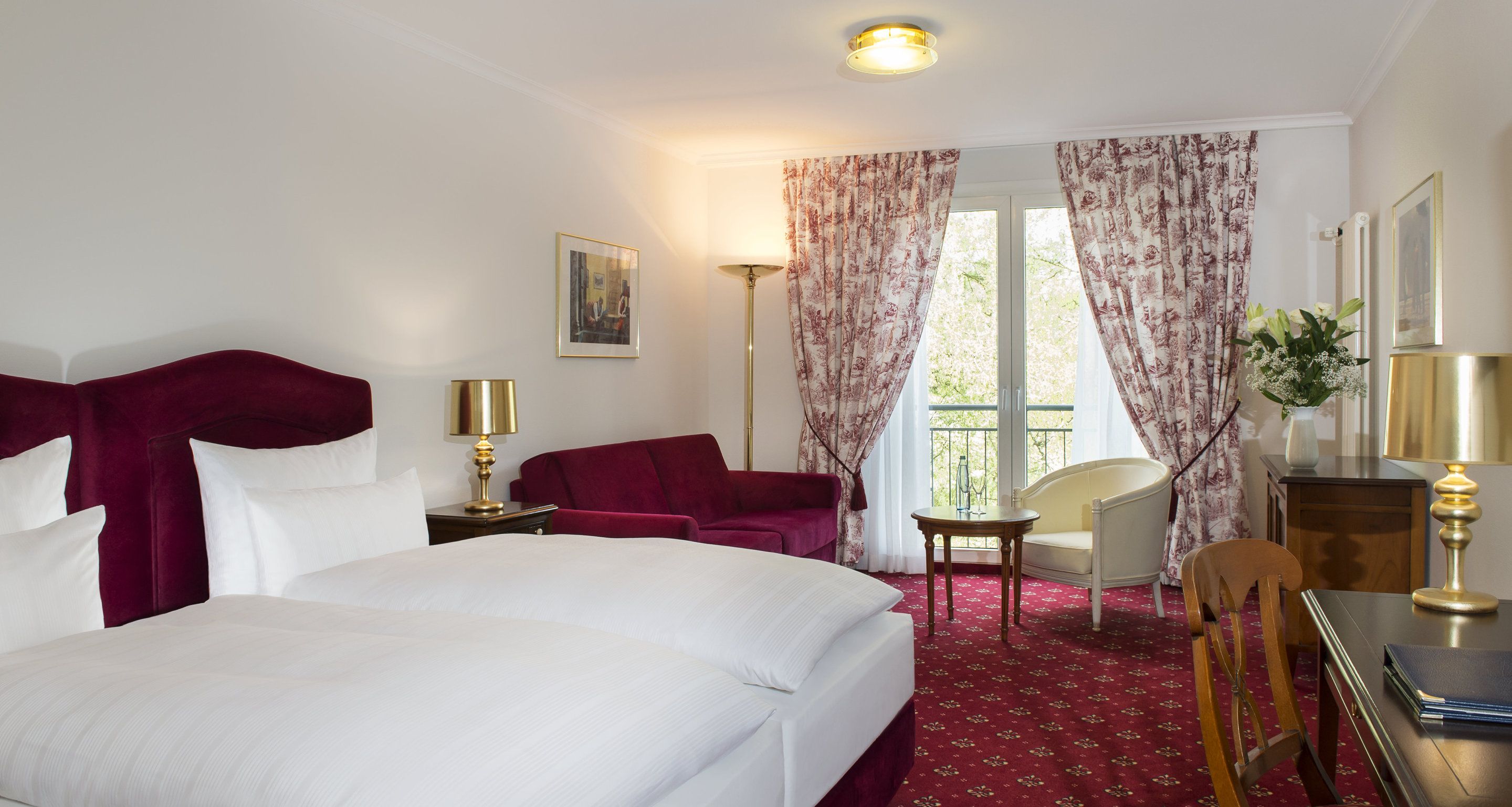 A hotel room with a large bed, two chairs, a desk, and a window with curtains.