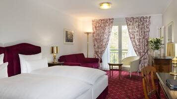 A hotel room with a large bed, two chairs, a desk, and a window with curtains.
