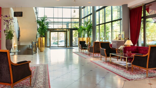 Un hall d’entrée spacieux, avec un canapé rouge, une table basse et une grande fenêtre donnant sur l’extérieur.
