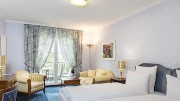 Une chambre d’hôtel avec un lit, deux fauteuils, un bureau, une lampe, un tableau au mur et une vue par la fenêtre.