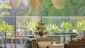 A restaurant with a view of greenery, wicker chairs, and a table with a centerpiece.