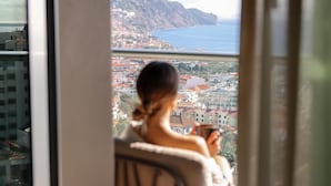 A person sitting by a window overlooking a coastal cityscape with buildings and a view of the sea.