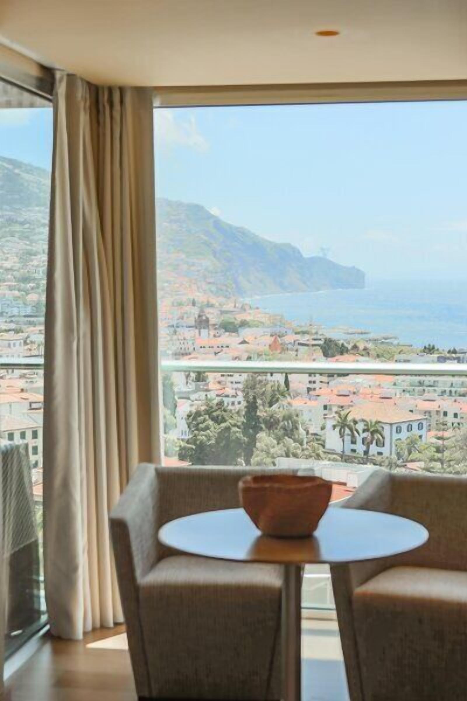 A room with a large window, a round table with a bowl, and two chairs.