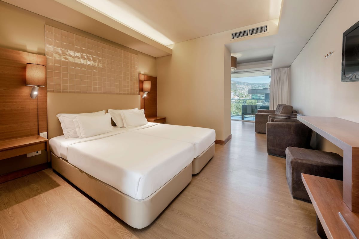 Une chambre d’hôtel moderne, dotée d’un grand lit, de lampes de chevet, d’un bureau et offrant une vue sur l’extérieur.