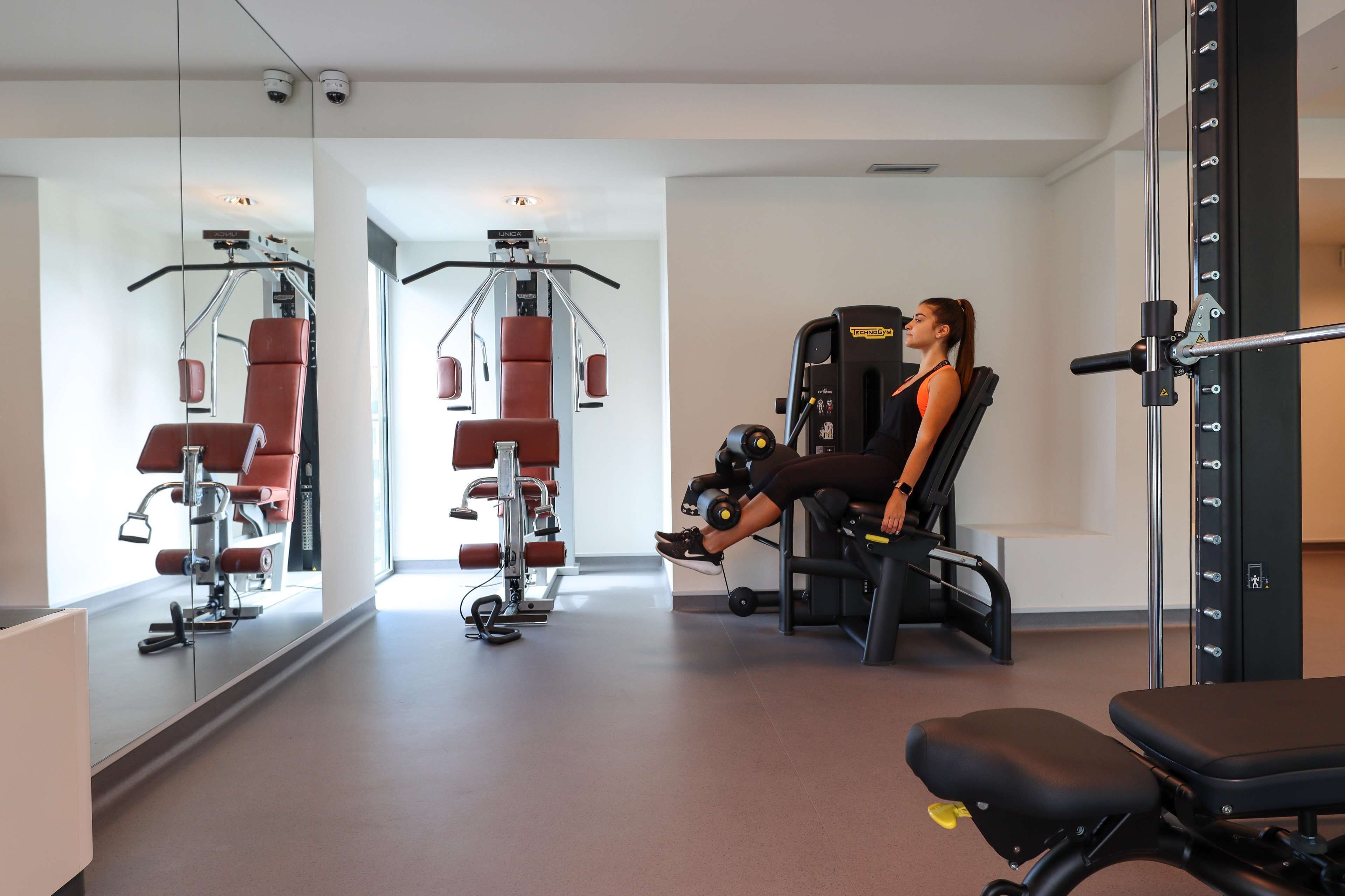 A modern gym with exercise equipment, a bench, and a mirror reflecting the space.