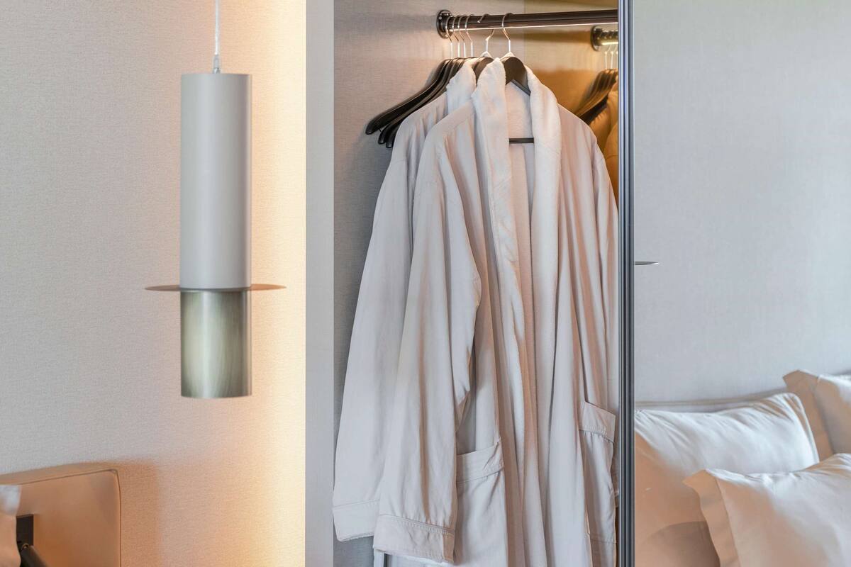 Une chambre d’hôtel moderne dotée d’un dressing, d’un pouf rond et d’un lit avec du linge de lit blanc.