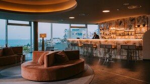 A modern bar area with a bar counter, seating, and a view of the ocean.