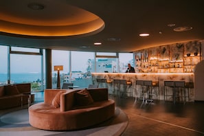 Un espace bar moderne doté d’un comptoir, de sièges et offrant une vue sur l’océan.
