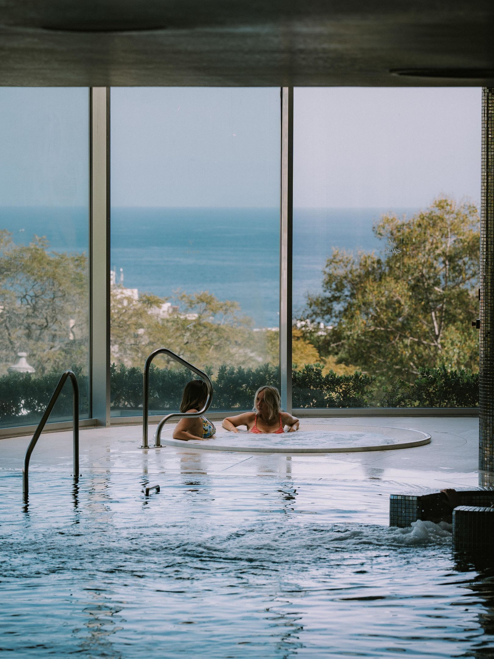 Ein Innenpool mit zwei Personen, großen Fenstern und Blick aufs Meer.