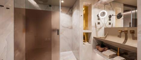 Un baño moderno con cabina de ducha de vidrio, tocador con un espejo grande y toallas dobladas ordenadamente sobre la encimera.