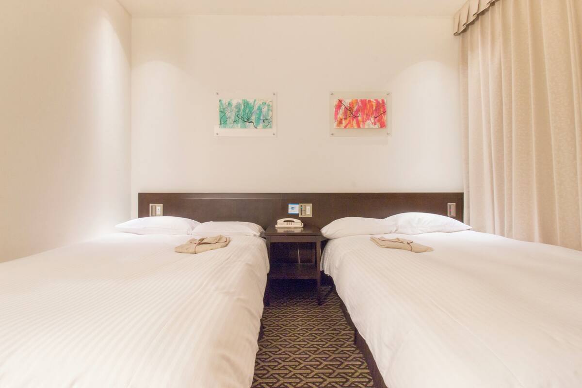 A hotel room with two beds, a nightstand, and two paintings on the wall.