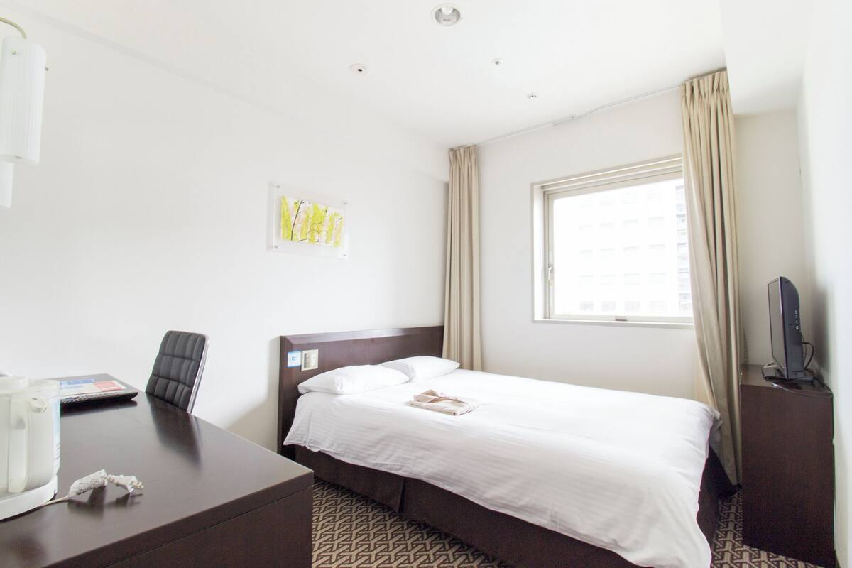 A hotel room with a bed, a desk, a chair, a television, and a window with curtains.