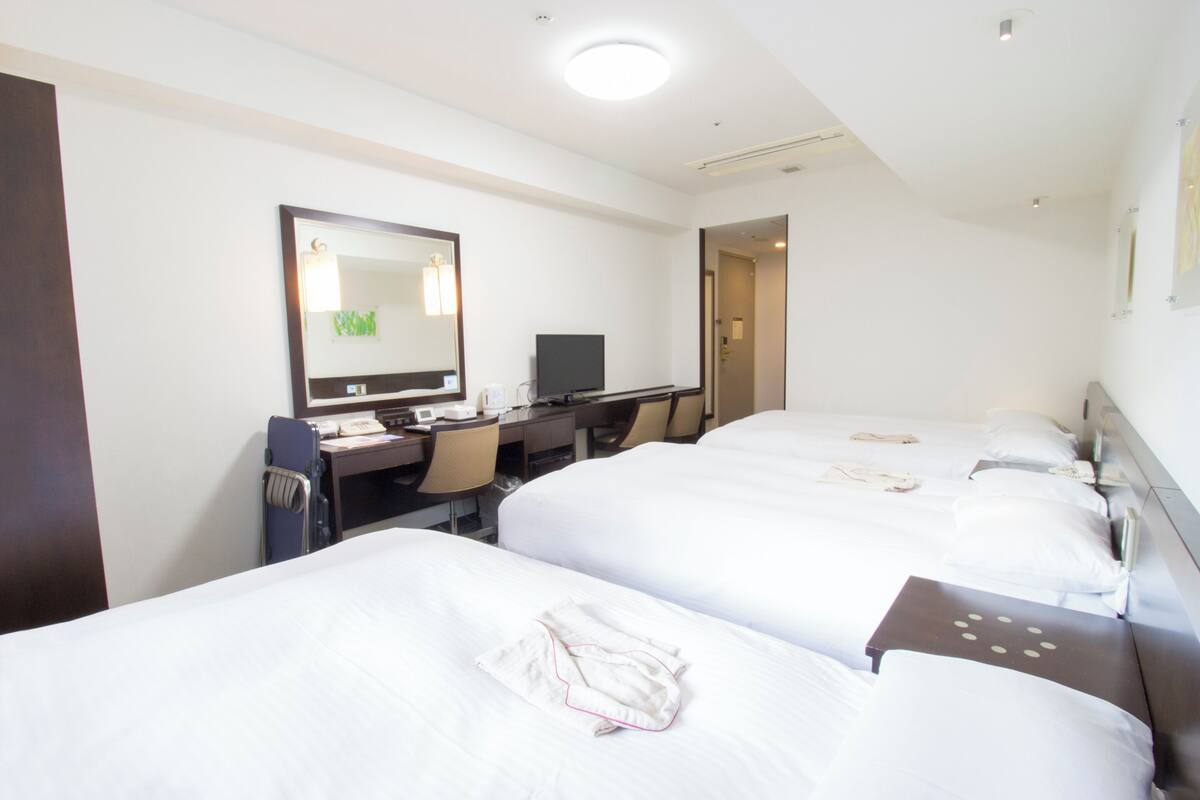 A hotel room with three beds, a desk with a computer, and a mirror.