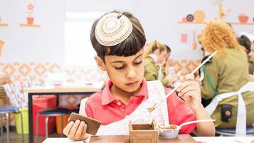 A child seated at a table with a snack, a tablet, and a drink.
