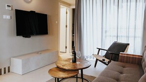 Un salon moderne avec un téléviseur à écran plat, un canapé, une table ronde en bois et une grande fenêtre avec des rideaux.