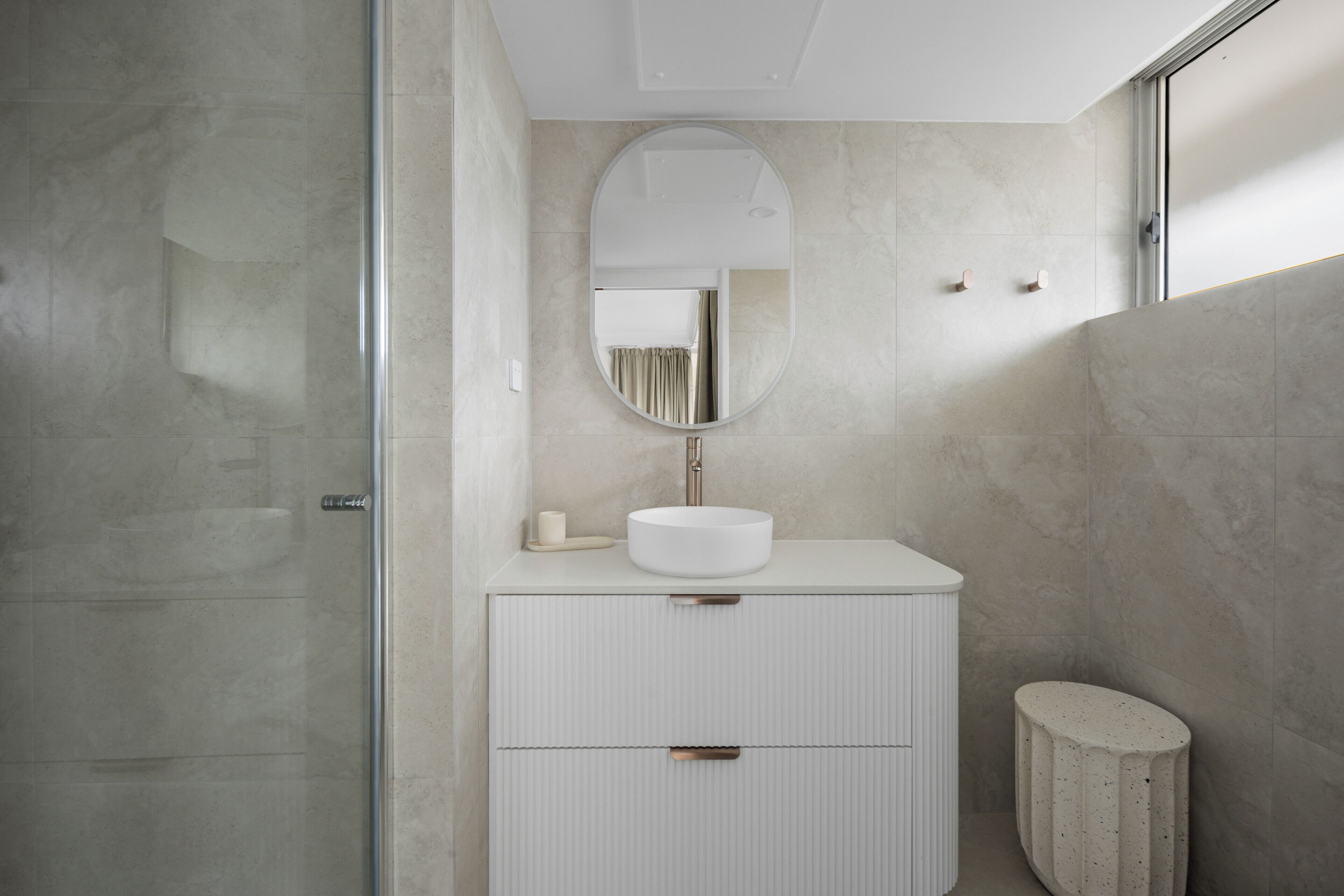 A modern bathroom with a round mirror, a white sink, and a small stool.