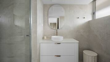 A modern bathroom with a round mirror, a white sink, and a small stool.