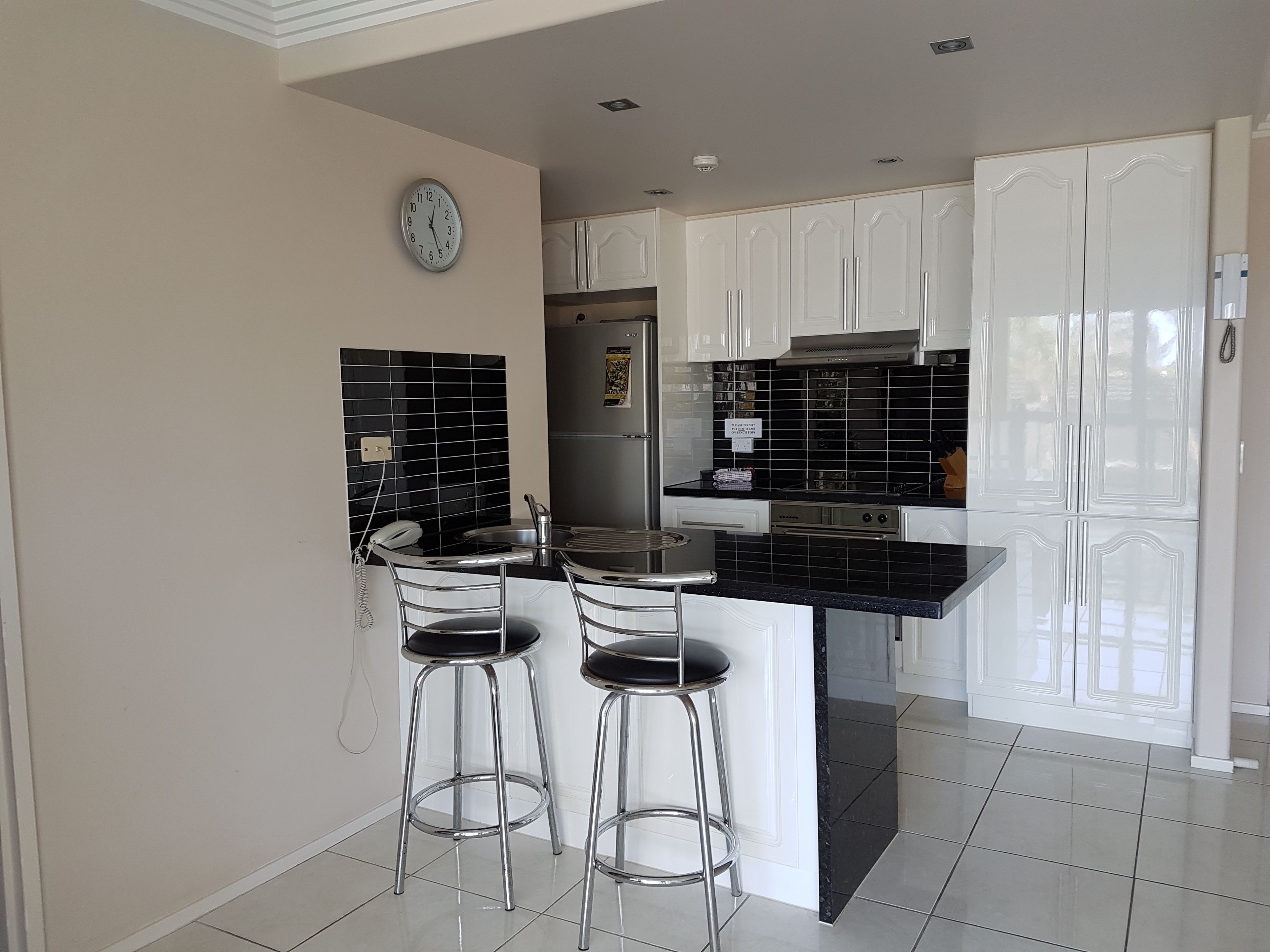 A modern kitchen with white cabinets, black countertops, and two bar stools.