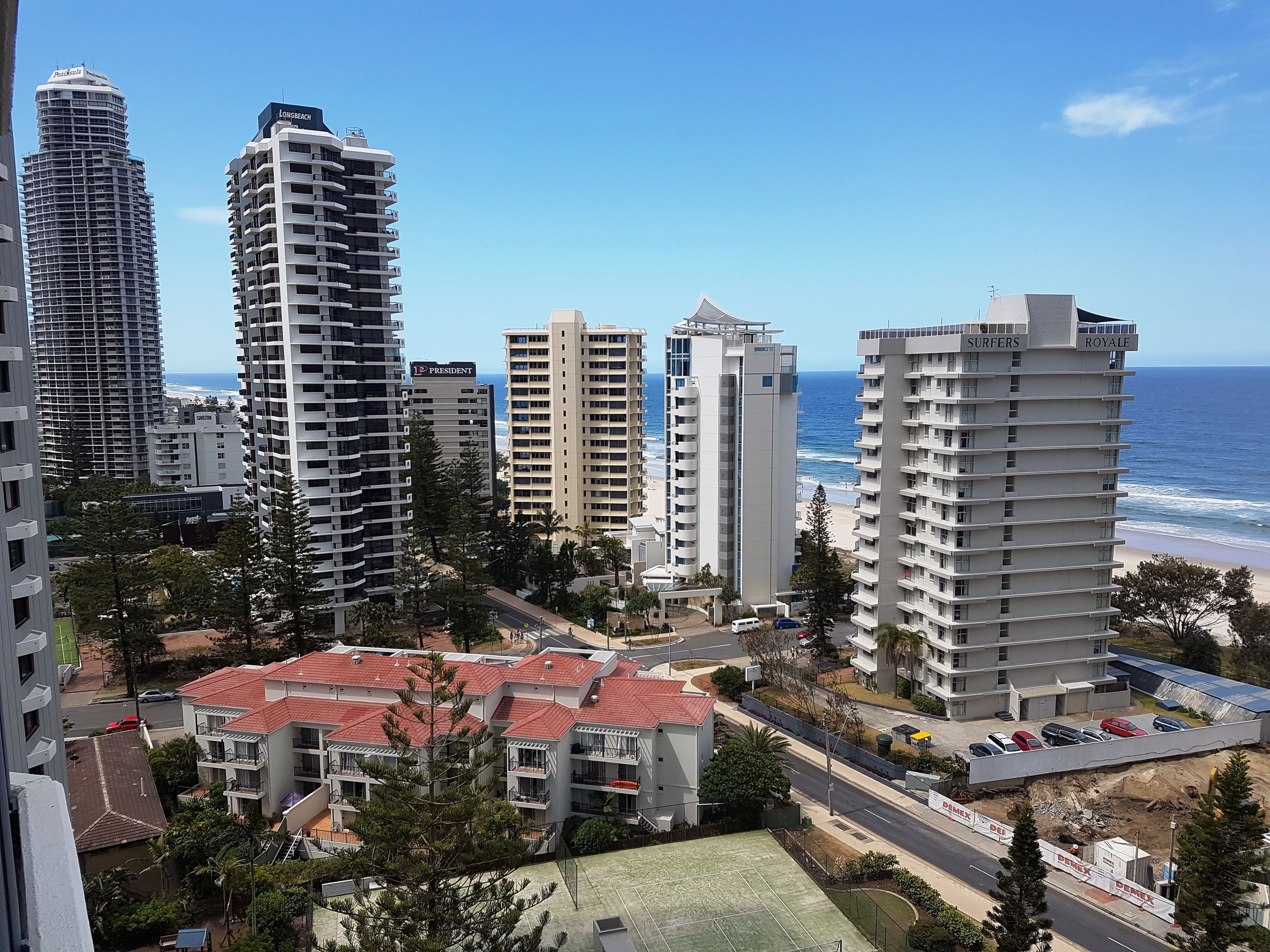 Eine Küstenstadtlandschaft mit Hochh äusern, darunter ein Hotel namens "Surfers Royale" mit Blick auf den Ozean.