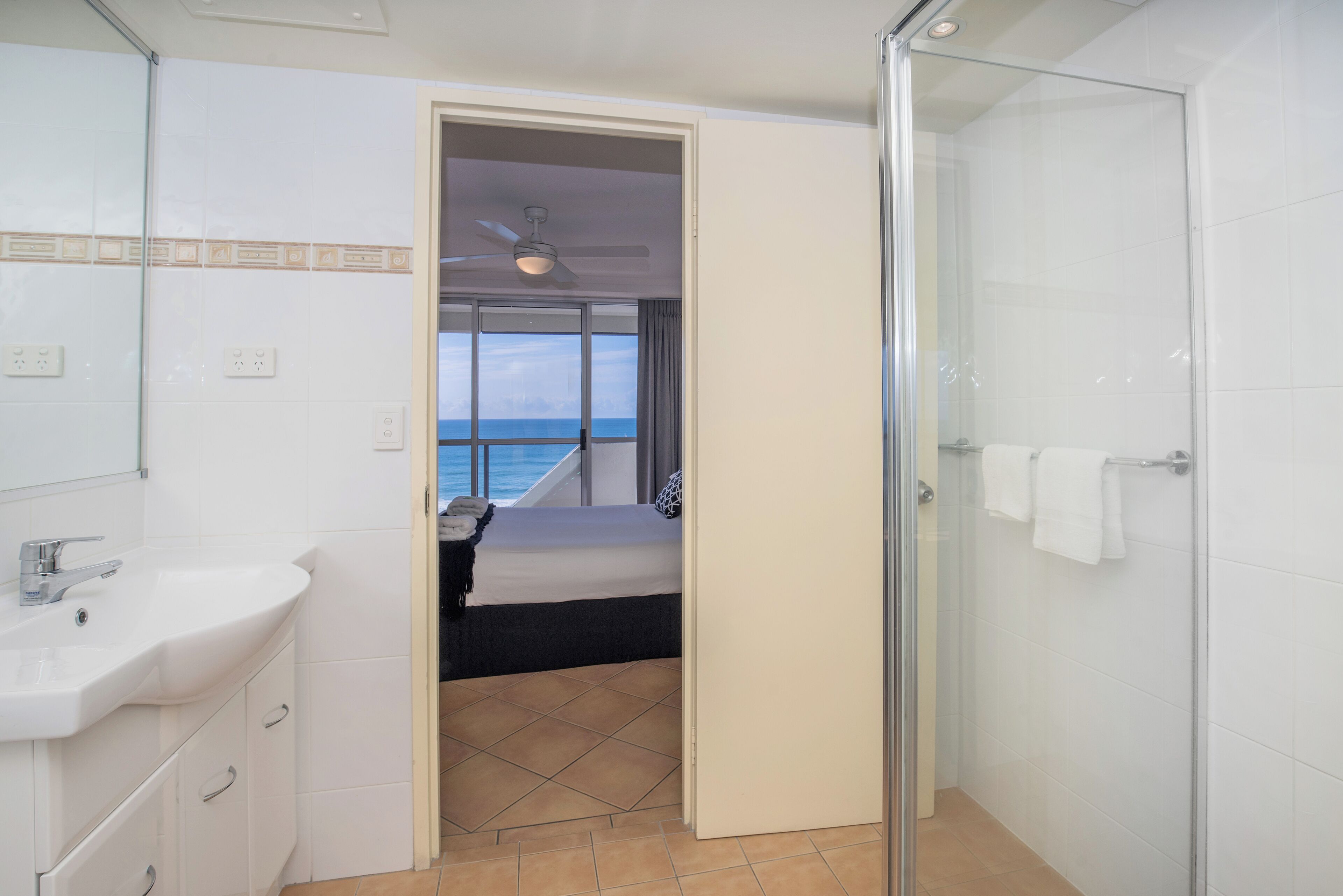 Une salle de bain avec une douche, un lavabo et une vue sur la mer par une fenêtre.