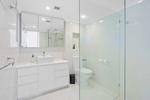 Un baño moderno con cabina de ducha de vidrio, un lavabo blanco y un inodoro.