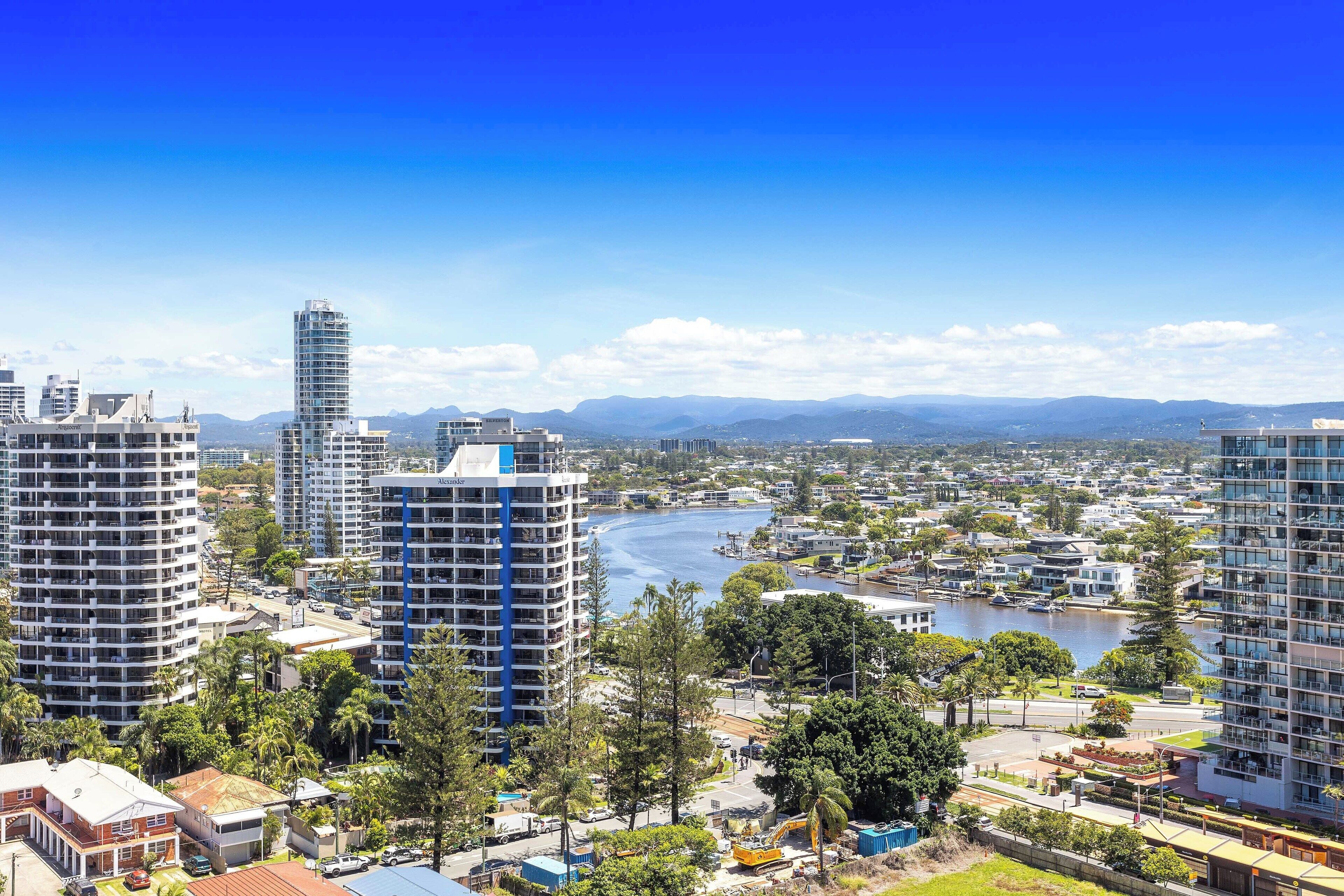 A high-rise building with a modern architectural design, surrounded by lush greenery and a river in the background.