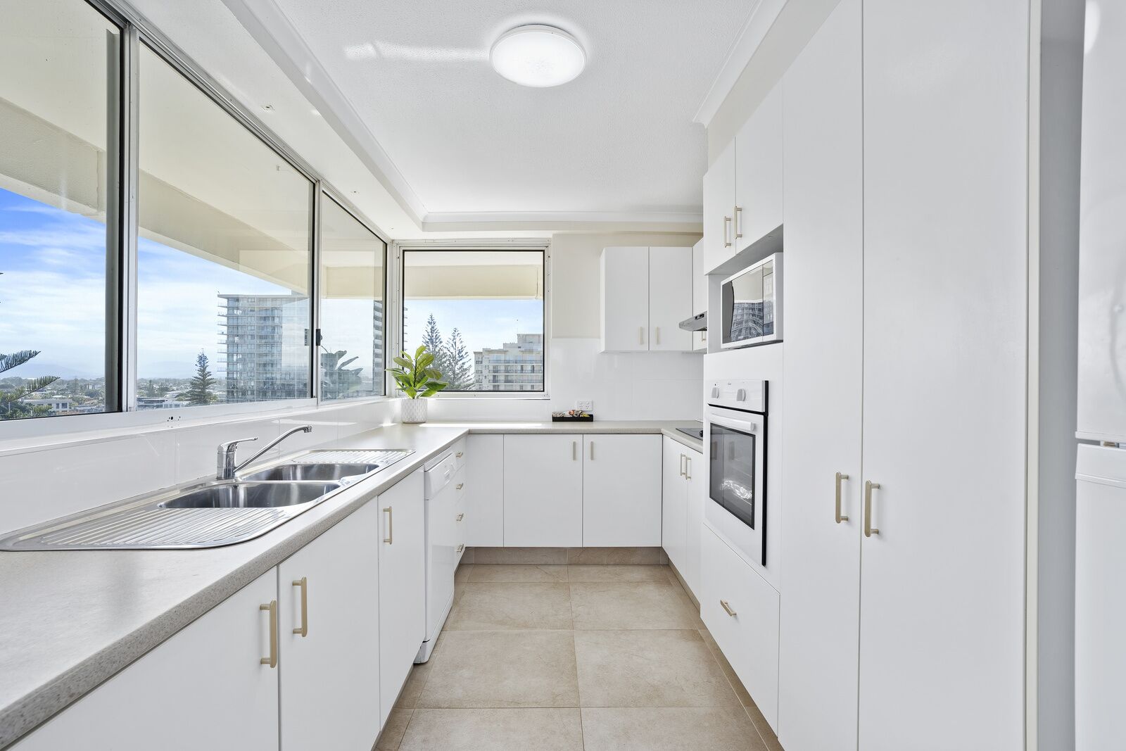 A modern kitchen with white cabinets, a stainless steel sink, and a window overlooking a cityscape.