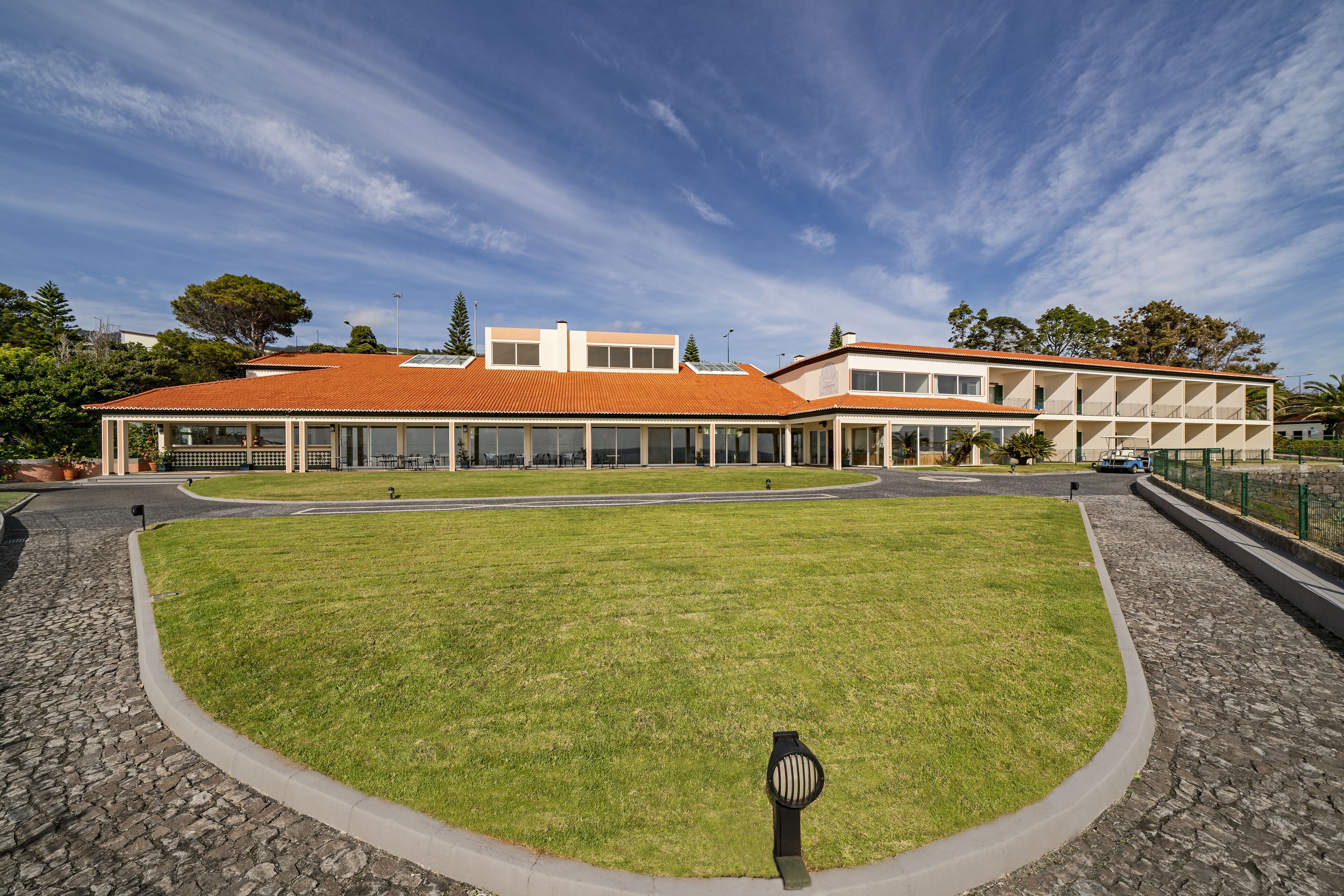 A building with a red-tiled roof, a central lawn, and a paved walkway.
