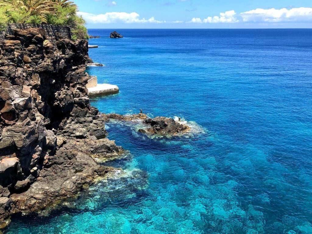 Un paisaje costero con aguas azules cristalinas, acantilados rocosos y un pequeño muelle.