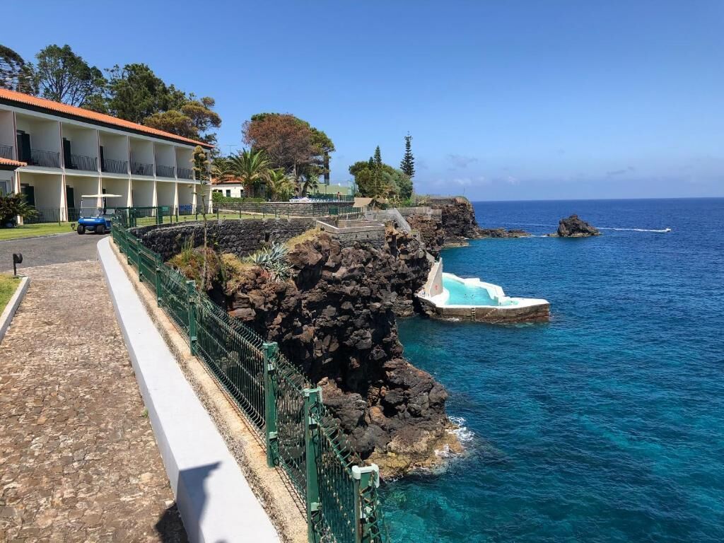 A coastal hotel with a rocky shoreline, a swimming pool, and a clear view of the ocean.